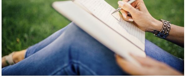 A person writing in a notebook while sitting on grass